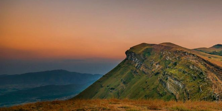 A majestic mountain with a grassy hill in the foreground, illuminated by a beautiful sunset.