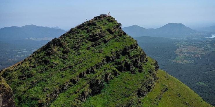 Man standing on mountain peak overlooking lush green valley.