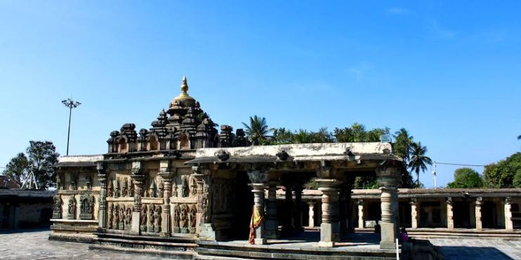 The Chennakesava Temple in Belur, surrounded by trees, is a large stone building with intricate carvings.