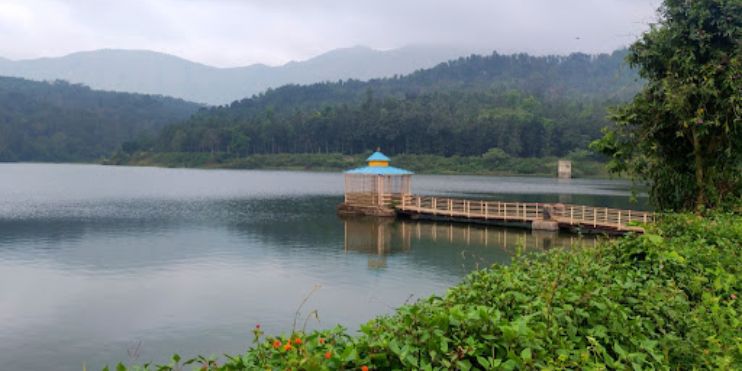 A wooden bridge over a serene lake with a small pavilion in the background.