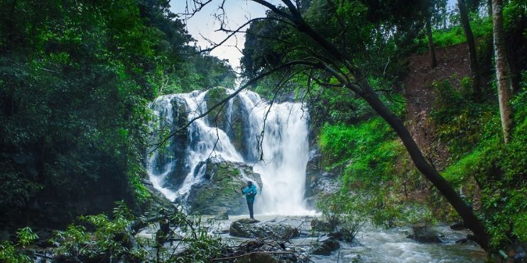 A man standing in front of Kodige Falls, a picturesque waterfall in the jungle, 15 km from Netravati Peak.