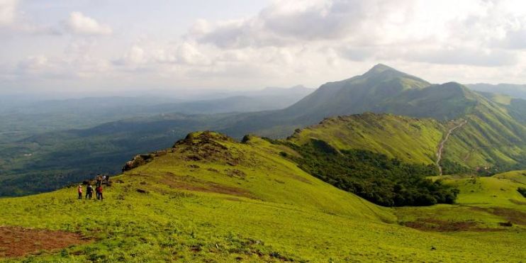 People walking on grassy hills of Mullayanagiri, the highest peak in Karnataka, offering stunning vistas and a peaceful environment.