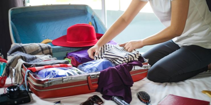 A woman sitting on a bed with an open suitcase, packing for a trip.