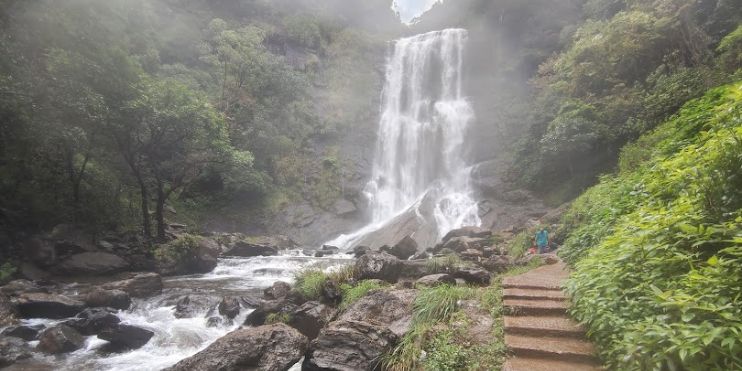 A man walking next to a waterfall on a scenic path.