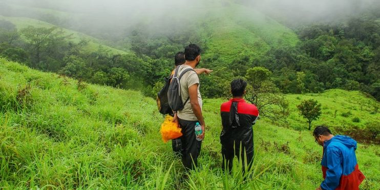 Three hikers standing on a foggy hillside, preparing to conquer Netravati Peak's challenging final segment.