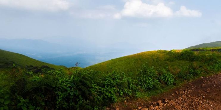 A dirt road winds through a hillside, surrounded by green grass and mountains, inviting exploration of the scenic landscape.