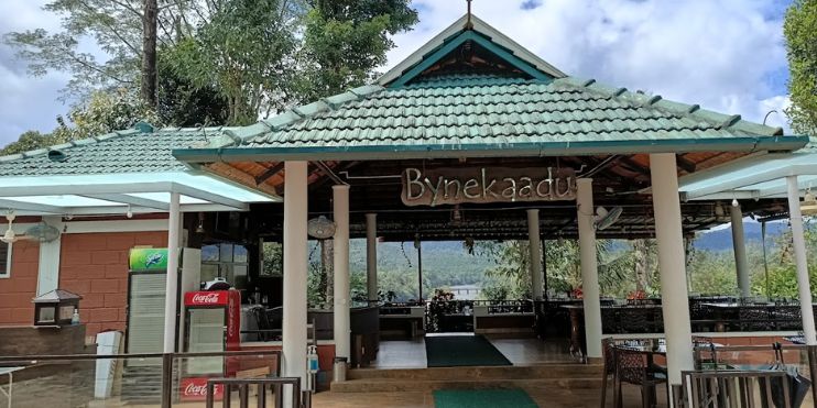 A restaurant with a green tiled roof, nestled among lush greenery near the serene Bhadra River, exuding rustic charm.