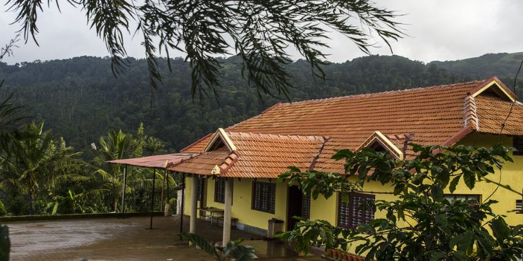 A yellow house with a red roof nestled in a lush green forest, embodying eco-friendly living in the Western Ghats.