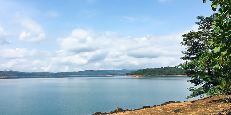 A serene view of Honnemaradu featuring a large body of water surrounded by a few trees under a clear sky.