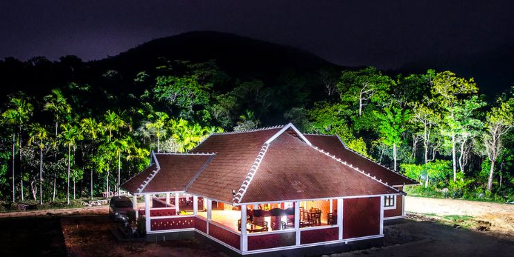 A small red house nestled in a lush forest, representing a luxurious homestay in Chikmagalur's serene landscape.