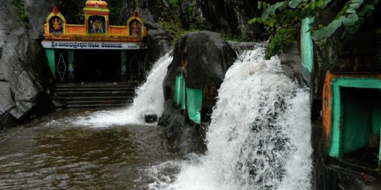 A stunning waterfall flows at the entrance of the ancient Veerabhadra Temple, surrounded by lush greenery and scenic beauty.