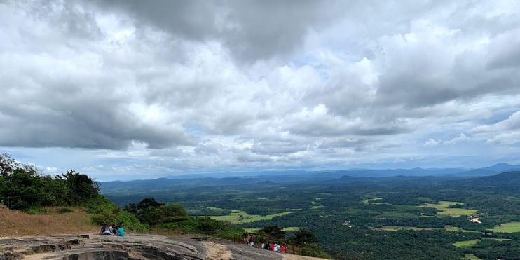 A group of people stands atop Kundadri Hill, gazing over the expansive valley below, surrounded by breathtaking scenery.