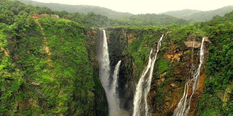  A large waterfall cascades through a lush green forest, resembling a string of pearls amidst the serene surroundings.