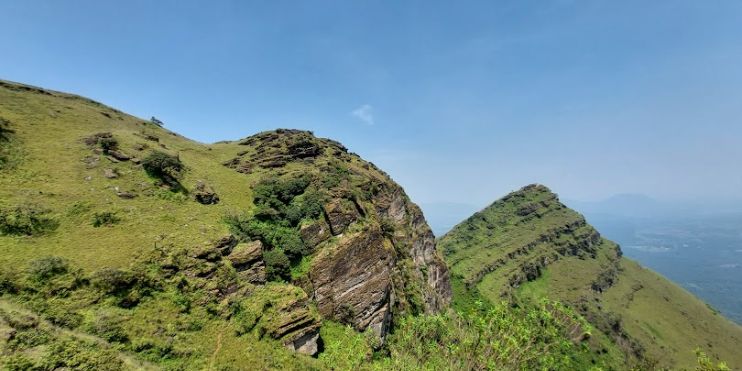 Panoramic view from Baba Budangiri summit, showcasing lush coffee estates and ancient caves amidst diverse mountain terrain.