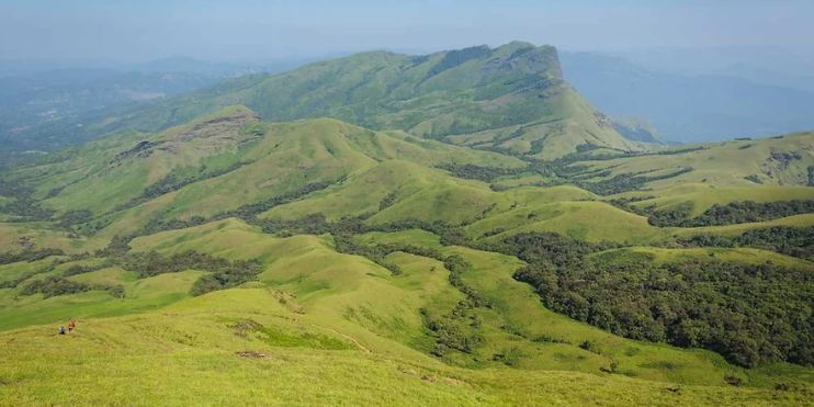 A breathtaking view from the summit of a mountain in India, showcasing lush valleys and distant hills under a clear sky.