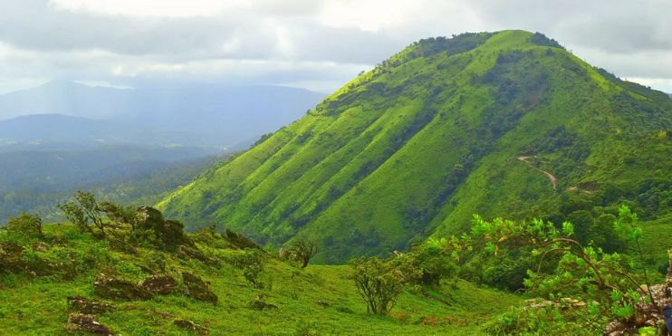 A scenic green mountain with a road atop, leading to Z Point in Chikmagalur, surrounded by lush Karnataka landscapes.