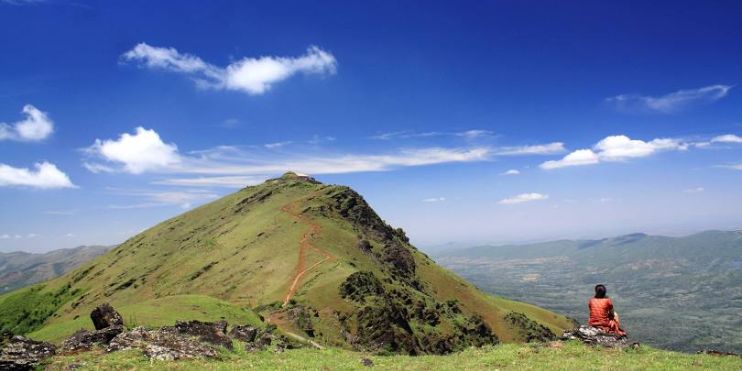 A man sits atop Mullayanagiri, Karnataka's highest peak, enjoying breathtaking views of hills and valleys below.