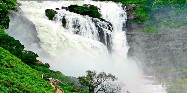 A majestic waterfall cascades down, embraced by lush green trees, creating a serene and picturesque natural setting.