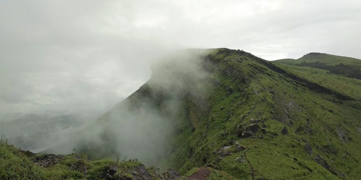 A serene mountain peak adorned with clouds and lush grass, embodying tranquility and natural beauty at Z Point, Chikmagalur.