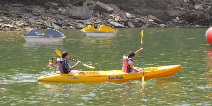 Two individuals paddling a yellow kayak on a serene water surface, surrounded by lush hills and forested landscapes.