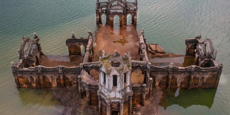 An aerial view of Shettihalli Church, showcasing its Gothic architecture amidst serene waters and intricate stone details.