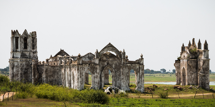 A large, old, abandoned church stands alone in a field, a remnant of its vibrant past and colonial heritage.