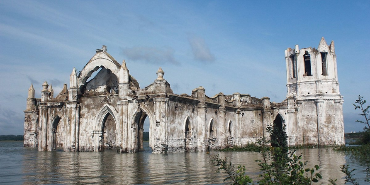 Ruins of a submerged church in a lake, partially visible during the monsoon, creating a mystical and atmospheric scene.