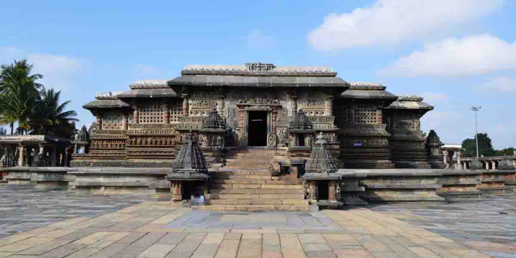 A stone temple surrounded by lush trees, showcasing intricate Hoysala architecture and rich historical significance.