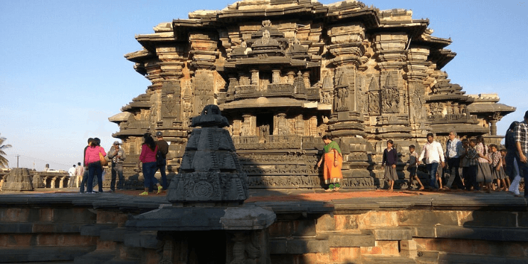 Tourists admire the intricate sculptures of the ancient Hoysaleswara Temple, a masterpiece of 12th-century Hoysala architecture.