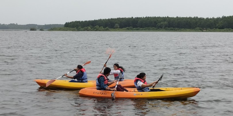 Three individuals kayaking on a serene lake, enjoying water sports at Yagachi Dam amidst beautiful surroundings.