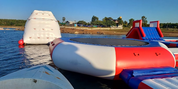 A large inflatable water park featuring a raft, surrounded by adventure activities like ziplining and trekking trails.