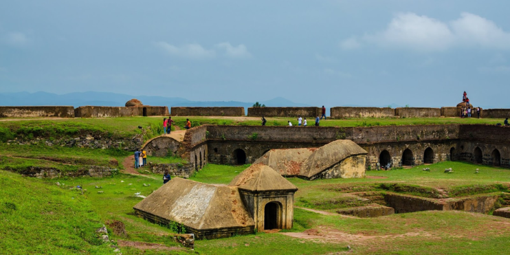 Ancient fort ruins stand amidst a lush green field, showcasing historical architecture and scenic beauty of the landscape.