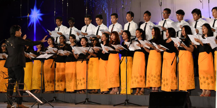 A choir performs Christmas carols on stage, creating a festive atmosphere with their harmonious voices.