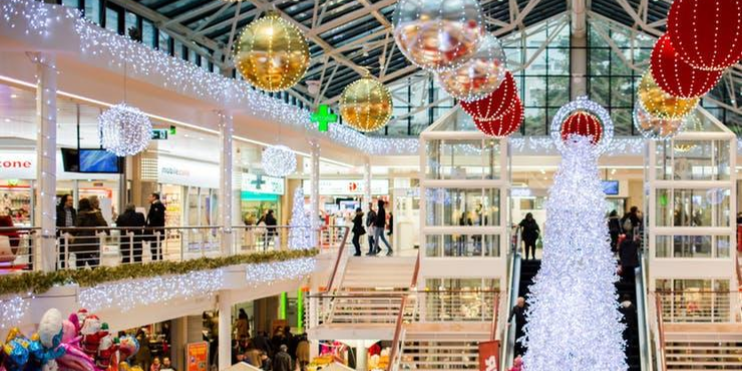 A beautifully decorated Christmas tree with vibrant lights is the centerpiece of a lively shopping mall.