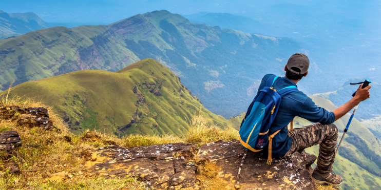 A man sits atop a mountain, equipped with a backpack and camera, enjoying the breathtaking view of nature.