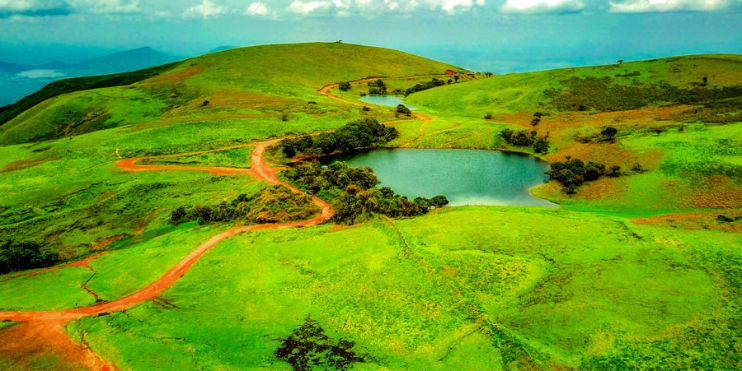 A serene green hill with a tranquil lake and a winding dirt road, perfect for nature lovers and outdoor enthusiasts.