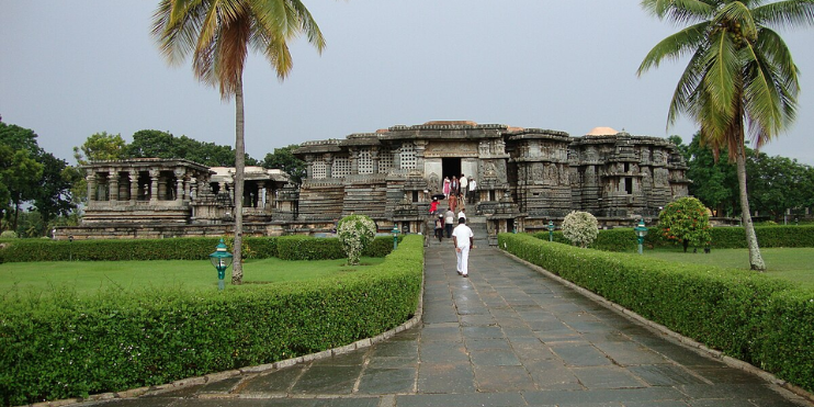 A man walks along a path leading to a temple, surrounded by lush greenery and historical architecture.