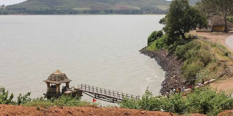 A bridge spans a tranquil body of water, leading to a quaint hut, surrounded by serene natural beauty.