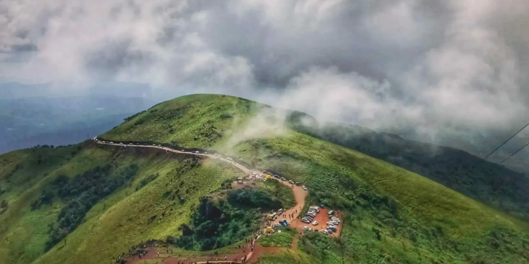 A scenic view of Mullayanagiri Peak, showcasing a winding road amidst lush landscapes and majestic mountain heights.