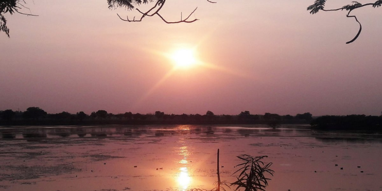 A serene sunset over a lake, framed by trees, highlighting the tranquil beauty of Davangere's natural landscape.