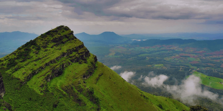 A mountain with green grass and clouds, representing the serene and spiritual landscape of Baba Budangiri.