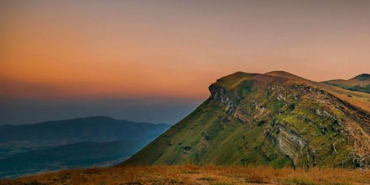 A scenic mountain with a grassy hill under a vibrant sunset, capturing the tranquil beauty of Kemmanagundi hill station.