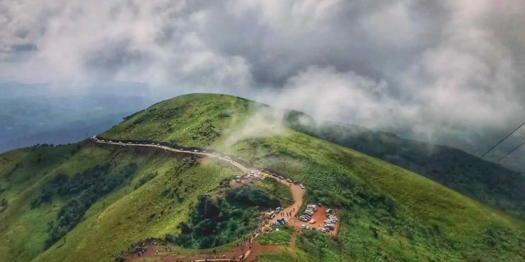 A scenic view of Mullayanagiri Peak, Karnataka, featuring a winding road atop the mountain surrounded by lush greenery.