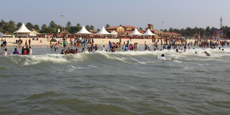 Crowded Malpe Beach with families enjoying the sun, water activities, and views of St. Mary's Island in the background.
