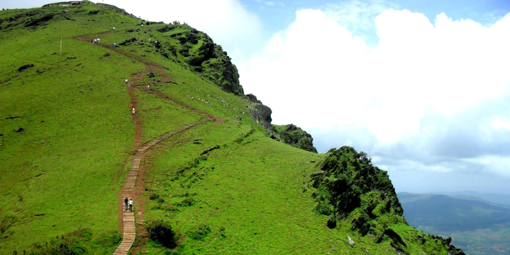 A scenic mountain path with hikers ascending, surrounded by rocky terrain and greenery, leading to the summit of Mullayanagiri.