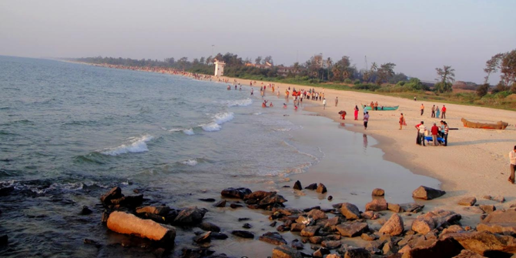 A lively Panambur Beach scene with people walking on sandy shores and rocky areas, showcasing its vibrant atmosphere.