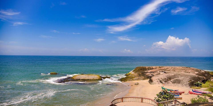 A serene beach with a rocky shore under a clear blue sky, evoking a mystical atmosphere at Someshwara Beach.