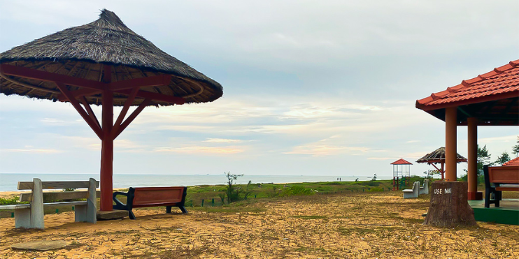 A serene Tannirbhavi Beach scene featuring a pavilion and a bench, surrounded by trees, ideal for relaxation and picnics.