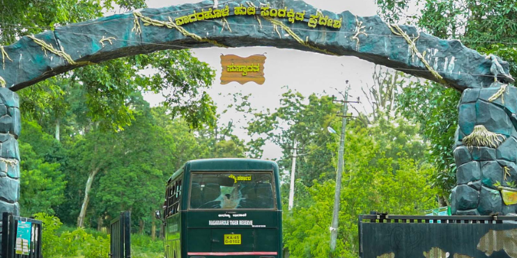 A green bus parked under a large arch at Kabini Wildlife Sanctuary, surrounded by lush greenery and scenic landscapes.