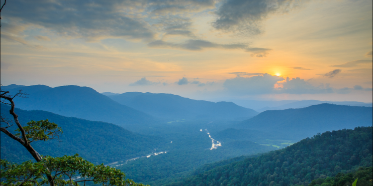 A sunset view of a valley surrounded by mountains, with vibrant colors illuminating the landscape.
